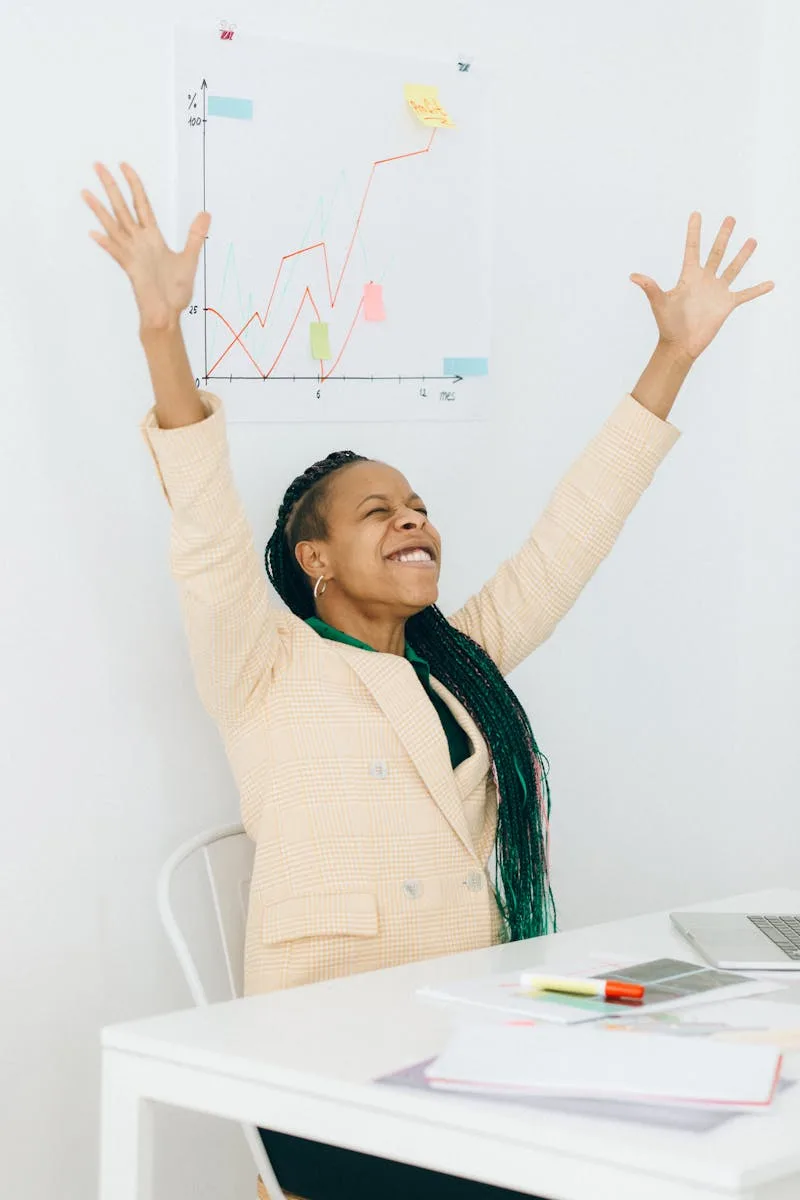 Confident businesswoman celebrates success with arms raised in office setting.
